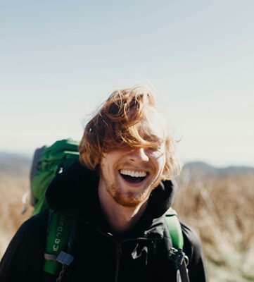 Smiling man hiking with a backpack and hair in his face after dental crowns in Encinitas.