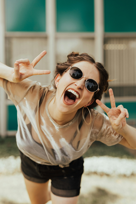 Smiling woman with perfect teeth poses with peace signs and sunglasses in Solana Beach